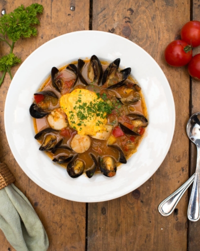 Overhead view of plated chowder bowl with mussels with napkin, cutlery and garnish